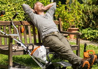 Un homme assis sur un banc dans son jardin entouré d'outils à batterie TSIHL